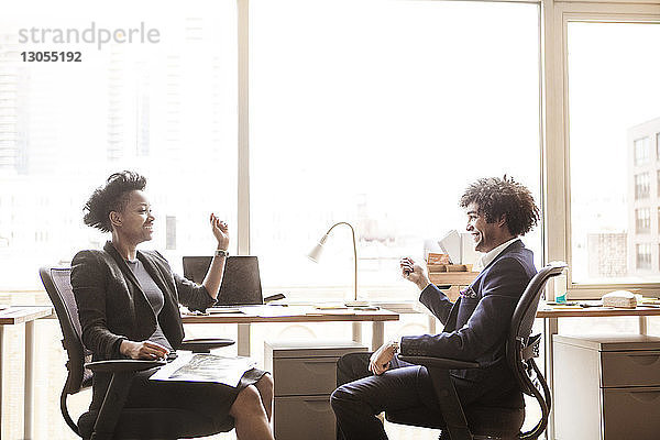 Glücklicher Geschäftsmann und Geschäftsfrau sitzen im Büro auf Stühlen