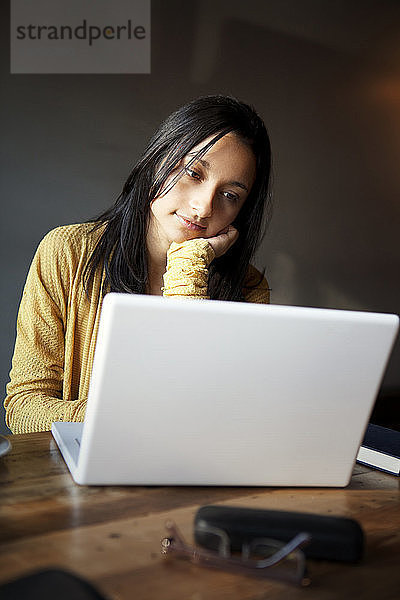 Nachdenkliche Frau benutzt Laptop  während sie im Haus am Tisch sitzt