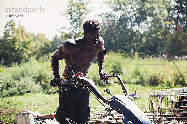 Junger Mann ohne Hemd  der auf dem Bauernhof arbeitet