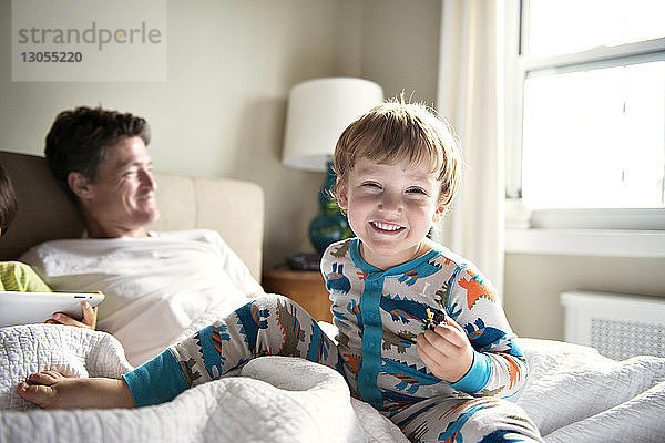 Glücklicher Junge genießt mit seinem Vater  während sein Bruder zu Hause am Bett einen Tablet-Computer benutzt