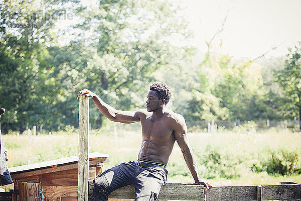 Nachdenklicher  muskulöser Mann  der an sonnigen Tagen auf Holz sitzt