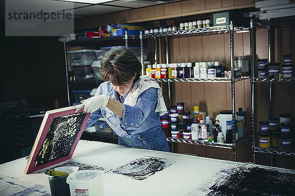 Handwerkerin untersucht Tintendrucke auf der Werkbank in einem Workshop