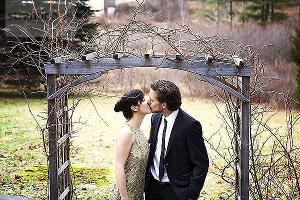 Pärchen küsst sich stehend am Holzeingang im Park