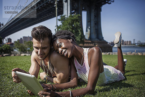 Glückliches Paar mit Tablet-Computer auf dem Feld liegend mit Manhattan Bridge im Hintergrund