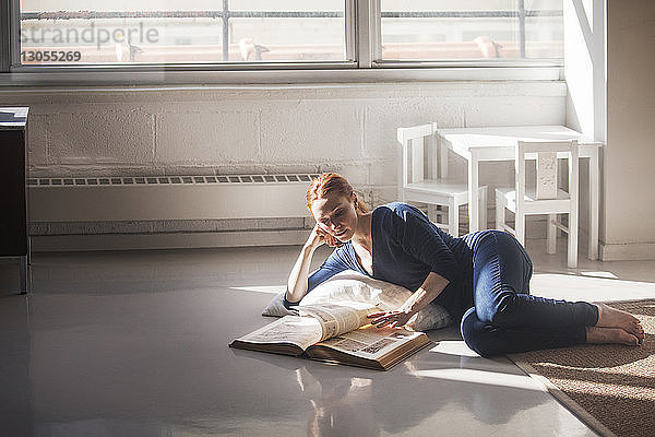 Frau liest Buch  während sie zu Hause auf dem Boden liegt