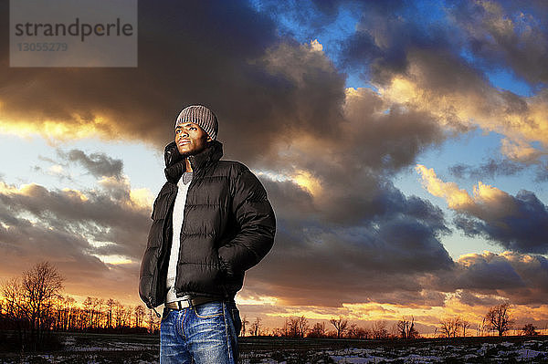 Nachdenklicher Mann steht bei Sonnenuntergang vor bewölktem Himmel