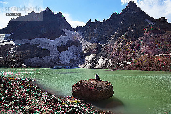 Fernsicht eines Wanderers auf einem Felsen am Seeufer gegen Berge