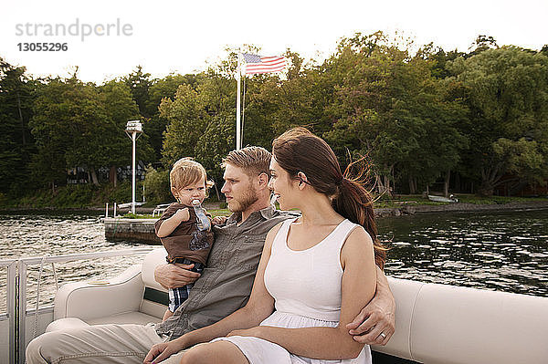 Mann trägt Sohn  während er mit Frau im Boot auf dem See Arm in Arm sitzt