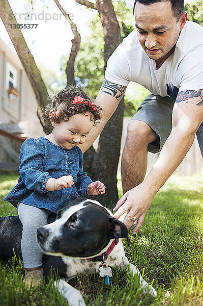 Vater hilft Mädchen  die auf einem Hund im Garten sitzt