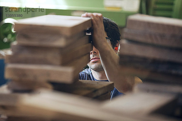 Männlicher Schreiner untersucht Holzbohlen in der Werkstatt