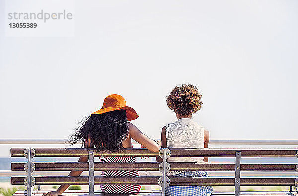 Freundinnen  die auf einer Bank am Meer sitzen