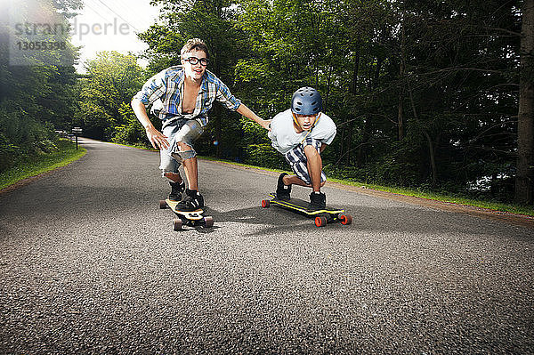 Jungen skateboarden auf der Straße inmitten von Bäumen