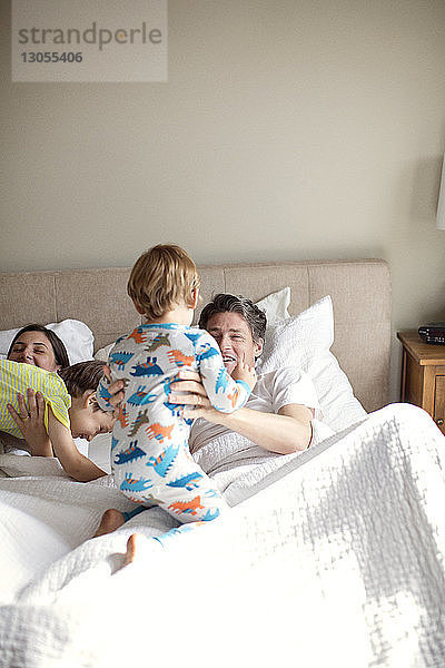 Glückliche Eltern spielen mit ihren Söhnen  während sie auf dem Bett liegen