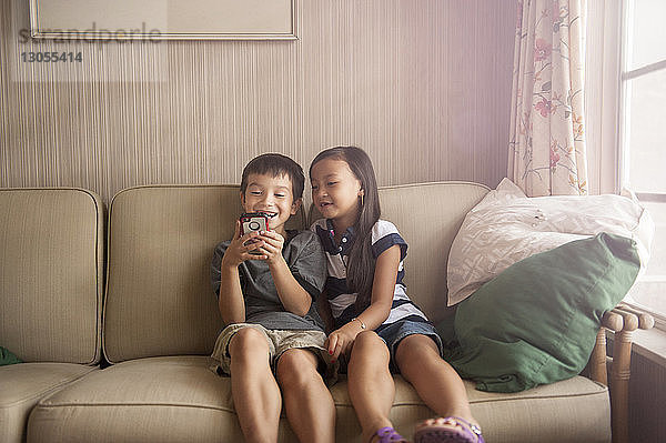 Lächelnde Geschwister telefonieren beim Entspannen auf dem Sofa