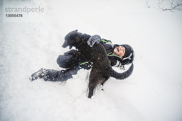 Draufsicht auf einen Jungen  der mit einem Hund auf einem schneebedeckten Feld spielt