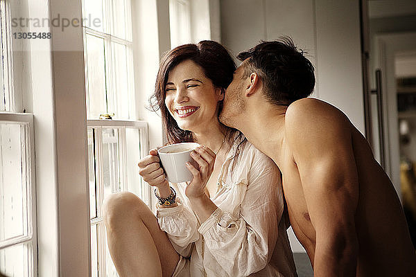 Fröhliches Paar genießt es  zu Hause am Fenster zu sitzen