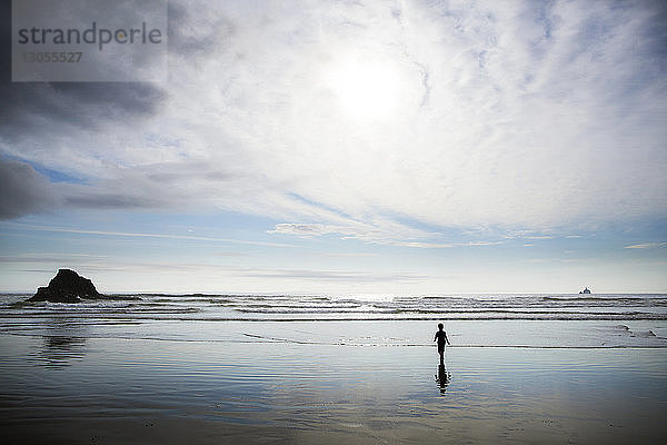 Junge geht am Strand am Ufer gegen bewölkten Himmel