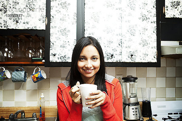 Porträt einer glücklichen jungen Frau mit Kaffeetasse in der Küche