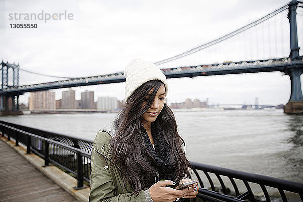 Frau telefoniert  während sie auf der Promenade gegen die Manhattan-Brücke in der Stadt steht