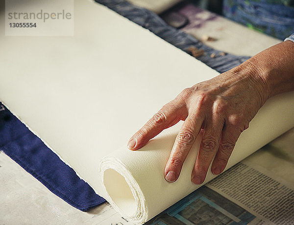 Ausgeschnittene Hände einer Handwerkerin beim Anpassen von aufgerolltem Papier auf Stoff in der Werkstatt