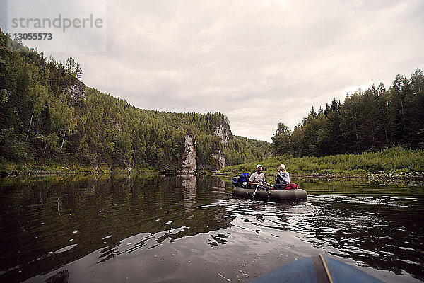 Junge Freunde beim River-Rafting gegen bewölkten Himmel