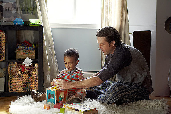 Vater und Sohn spielen zu Hause auf dem Teppich sitzend mit Spielzeugklötzen