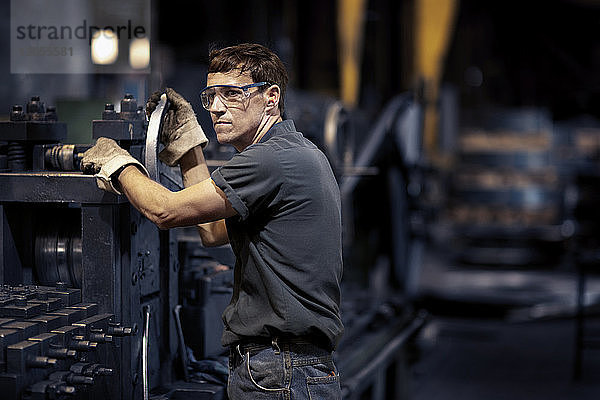 Arbeiter schaut weg  während er an Maschinen in der Metallindustrie steht