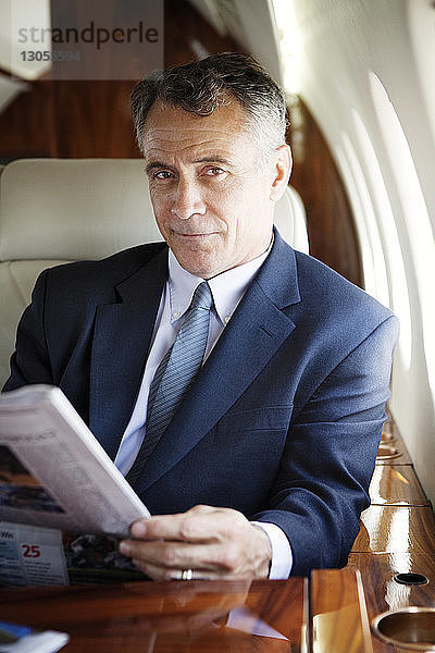 Porträt eines selbstbewussten Geschäftsmannes  der eine Zeitung in der Hand hält  während er im Firmenjet reist
