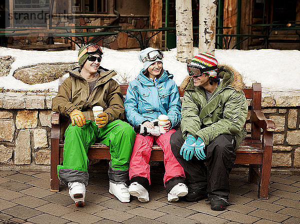 Glückliche Skifahrer sitzen auf der Bank im Skigebiet