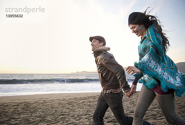 Glückliches junges Paar hält sich an den Händen und geht am Strand
