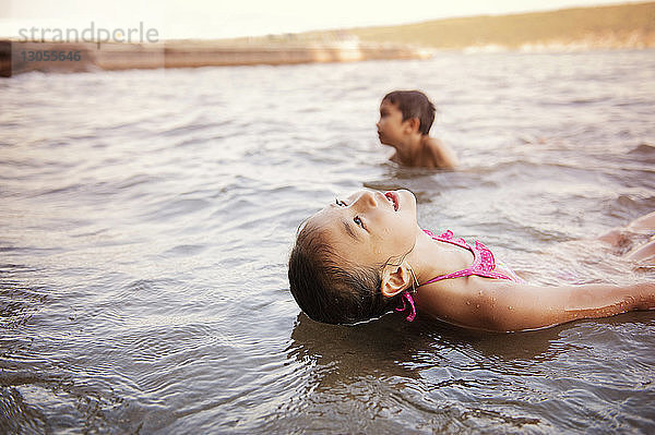 Mädchen entspannt sich im See mit Bruder im Hintergrund