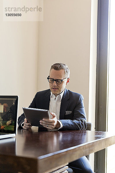 Geschäftsmann benutzt Tablet-Computer  während er im Büro am Tisch sitzt