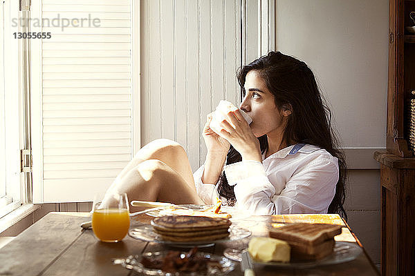Nachdenkliche Frau trinkt zu Hause Kaffee am Frühstückstisch