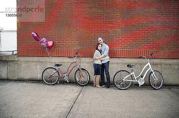 Junges Paar umarmt sich  während es inmitten von Fahrrädern auf der Straße an der Wand steht
