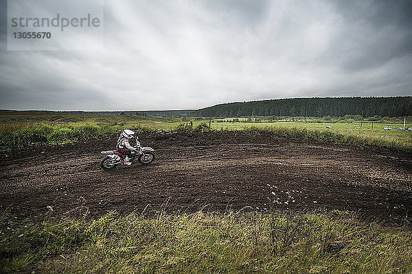 Motorradfahrer fährt mit Geländefahrrädern auf Feld gegen bewölkten Himmel