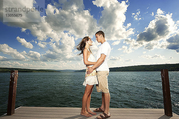 Seitenansicht eines jungen Paares  das sich auf dem Steg über dem See gegen den Himmel anschaut