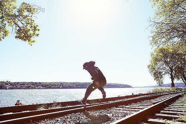 Mann springt auf Eisenbahnschienen am Fluss gegen klaren Himmel