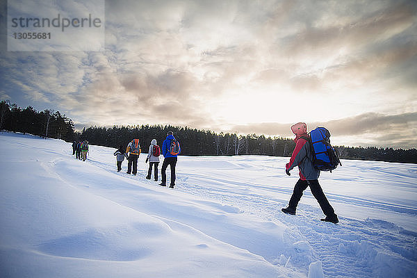 Freunde wandern auf schneebedecktem Feld gegen wolkigen Himmel