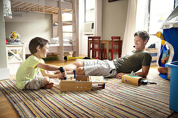 Glücklicher Vater schaut dem Jungen zu  der zu Hause mit Spielzeug spielt