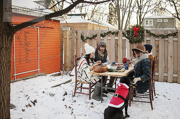 Freunde genießen bei Tisch und im schneebedeckten Hinterhof