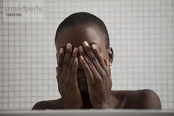 Nahaufnahme einer Frau  die im Badezimmer das Gesicht mit den Händen bedeckt