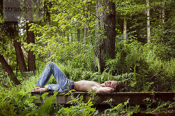 Mann ohne Hemd auf Pier im Wald liegend