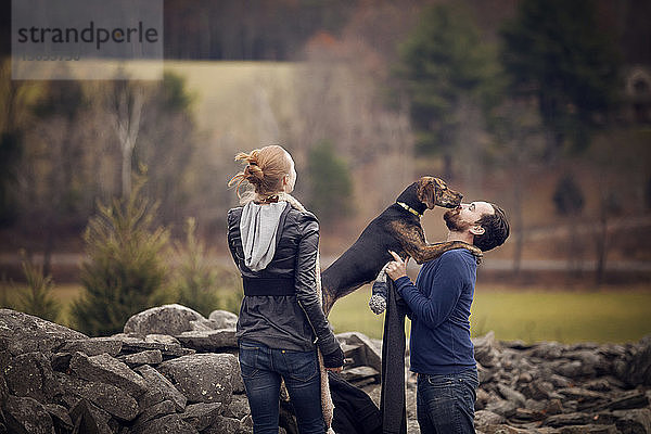 Frau schaut Mann spielt mit Hund an Steinmauer