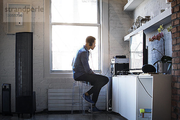 Seitenansicht eines Mannes  der Musik hört  während er zu Hause am Fenster sitzt