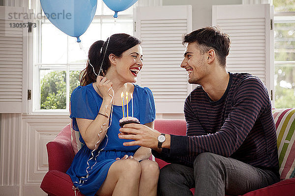 Glückliches Paar feiert Geburtstag  während es zu Hause auf dem Sofa sitzt