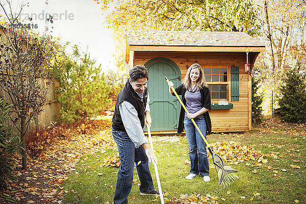Glückliches Paar reinigt Herbstlaub auf Grasfeld