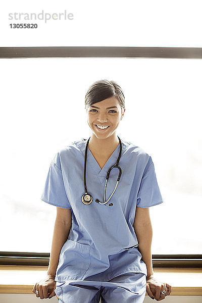 Porträt einer lächelnden Ärztin auf dem Fensterbrett sitzend