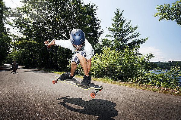 Junge skateboardet über Straße gegen Bäume an sonnigem Tag