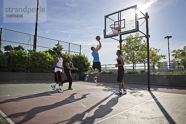 Freunde spielen an einem sonnigen Tag Basketball auf dem Platz