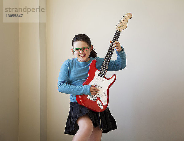 Fröhliches Mädchen spielt zu Hause Gitarre an der Wand